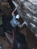 Person climbing a rock wall with climbing gear on the ground.