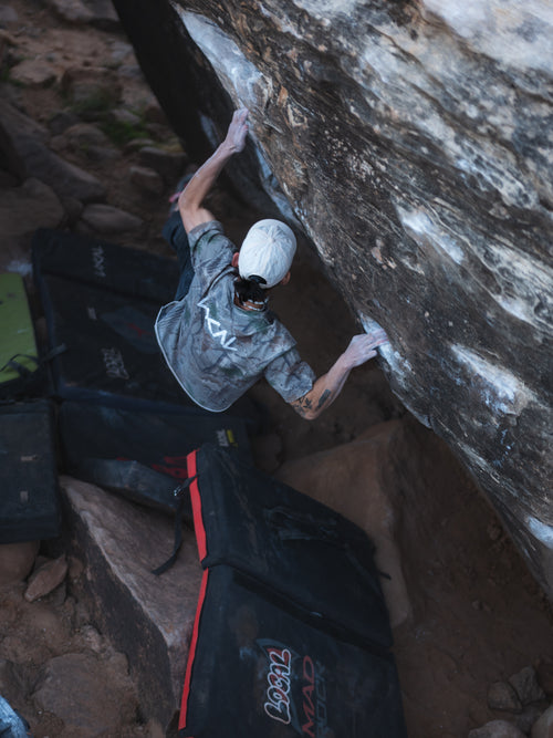 Person climbing a rock wall with climbing gear on the ground.