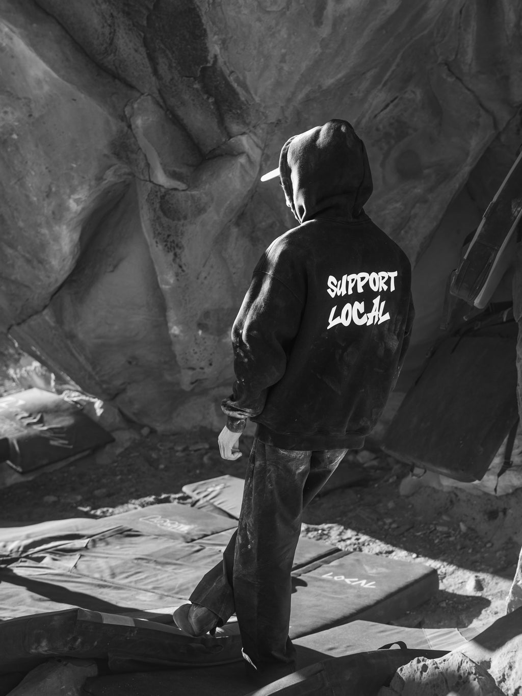 Person wearing a hoodie with 'Support Local' text in a rocky outdoor setting